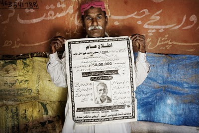 Manu Bheel with a poster listing the names of his missing family members in Pakistan