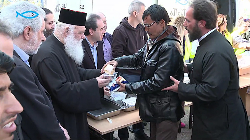 Archbishop Hieronymus of Athens and All Greece is pictured distributing food to migrants at the Port of Piraeus. The Archbishop removed his cross from his vestments during the visit to Piraeus, in order, he said, not to "offend" the Muslim migrants. (Image source: HellasNewsTv video screenshot)